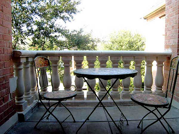Balcony with ornate balustrade, wrought iron table and chairs against brick wall.