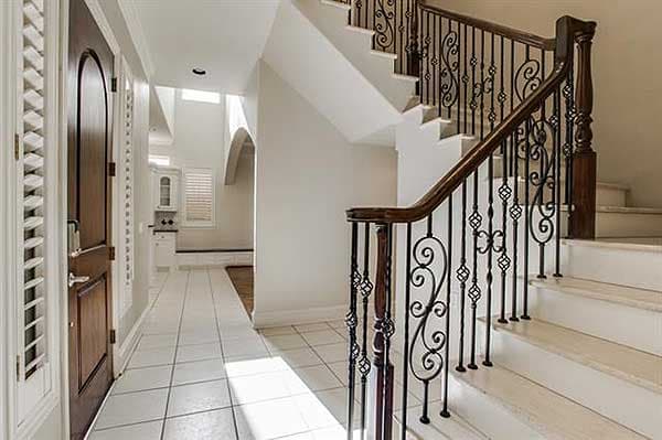 Interior view of a foyer with a grand staircase featuring a wooden handrail and decorative metal balusters. A wood front door is visible on the left.