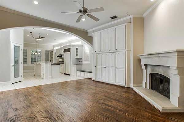 Living area with fireplace and built-in cabinetry opens to a kitchen with island and white cabinets.