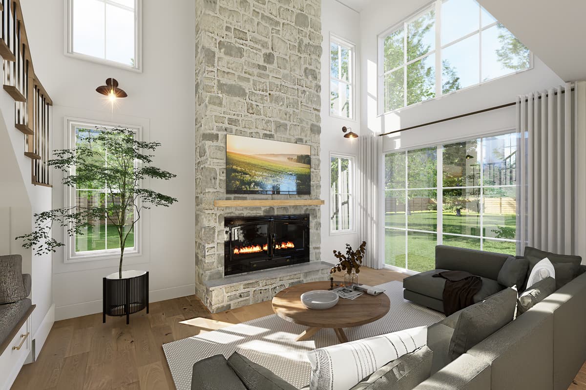 A modern living room with a stone fireplace, large windows, and a comfortable sectional sofa. A tree in a decorative pot sits near a window.
