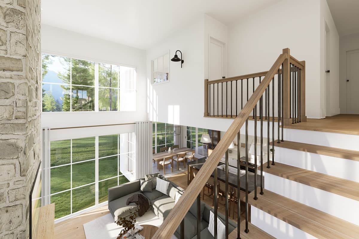 An open-concept living space with a high ceiling, large windows, and a staircase leading to a loft area. A modern sofa and dining table are visible.