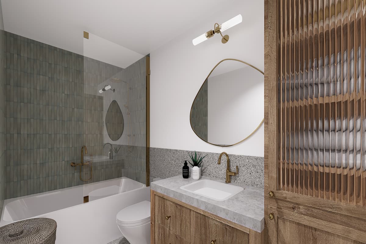 Modern bathroom with a bathtub, toilet, and vanity featuring brass fixtures, an organic-shaped mirror, and wooden cabinet with a textured door.