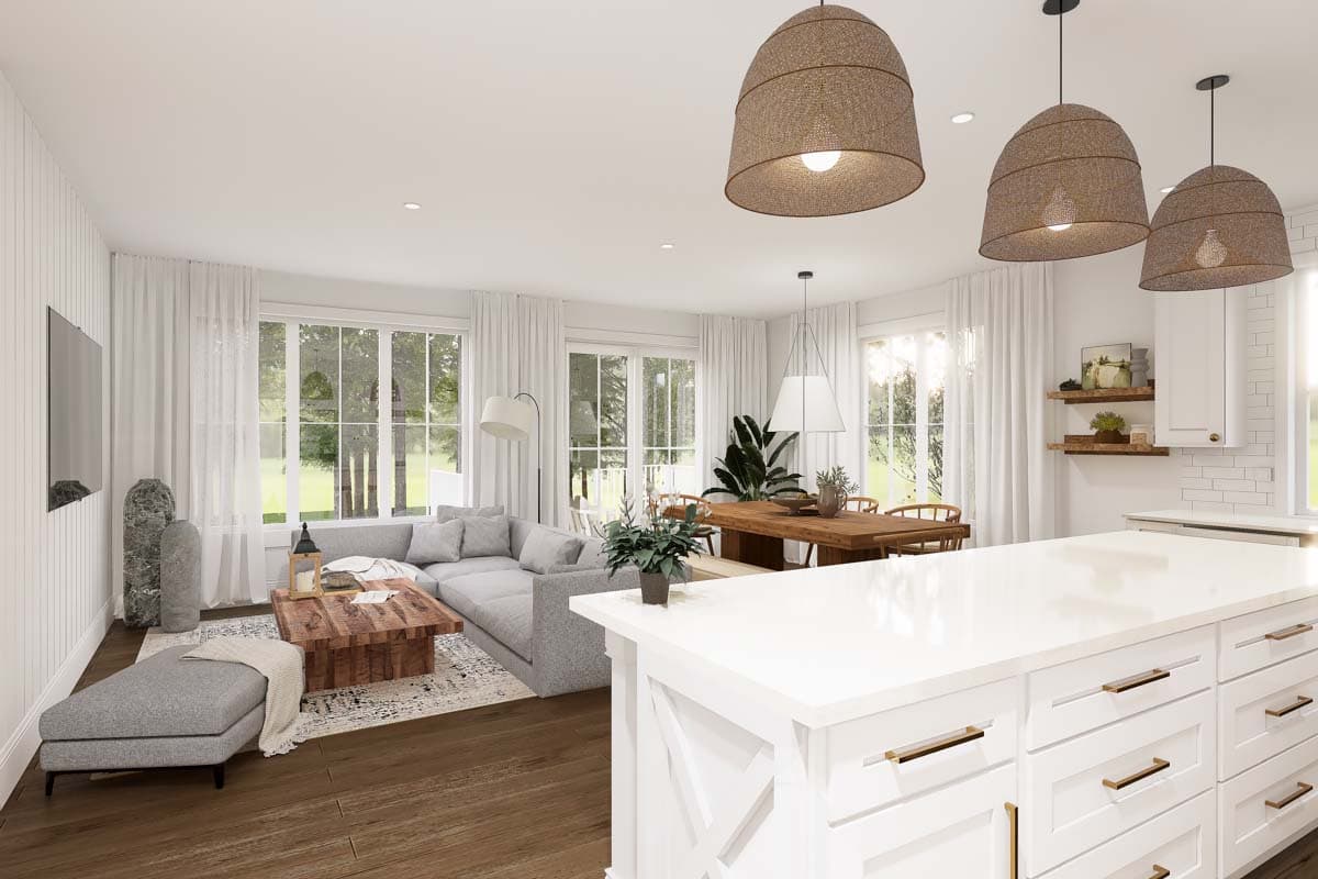 Open concept living, dining, and kitchen area with sectional sofa, wooden dining table, and kitchen island with white counters.