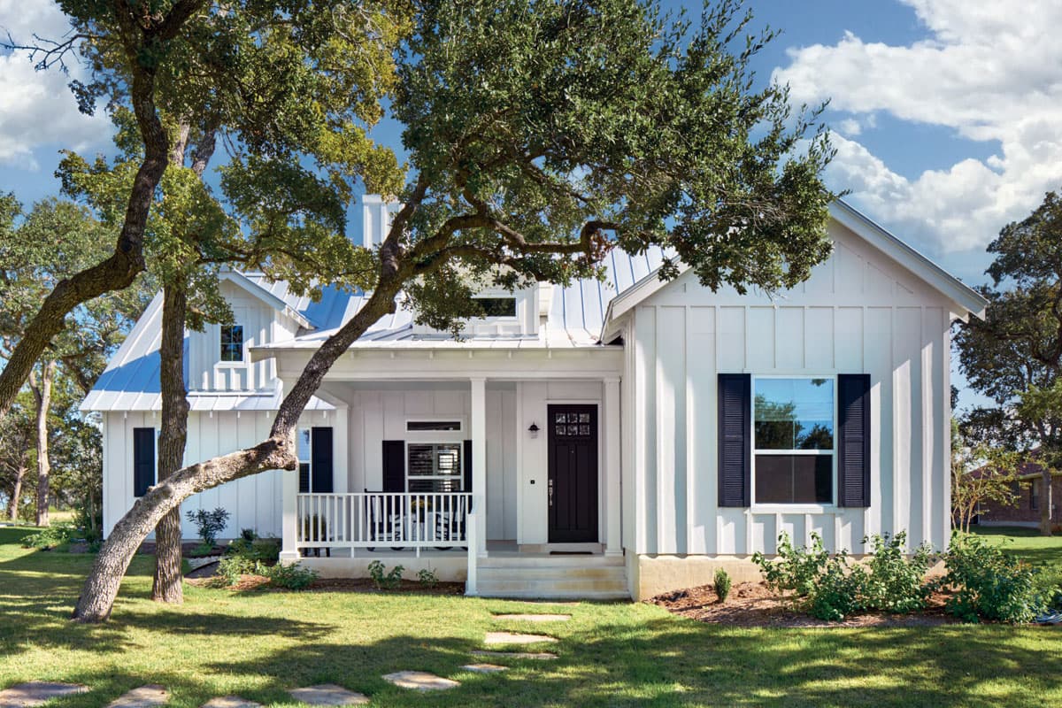 House plan exterior: Farmhouse style with a front porch, gabled roof, and two stories. Features include dark shutters and a metal roof.