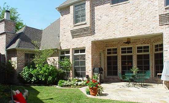 House plan exterior with brick facade, multiple gables, a covered patio with large windows, and a prominent chimney.