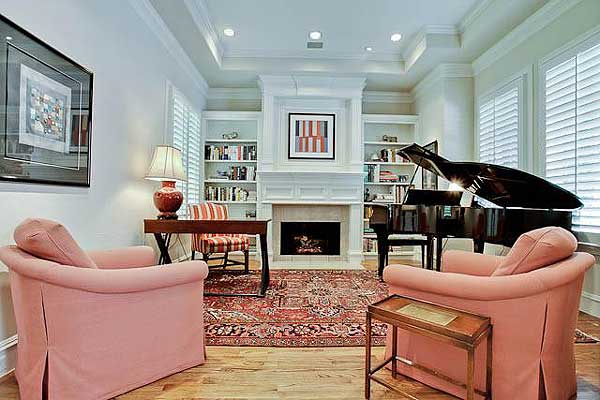 Living room interior with fireplace, bookshelves, a grand piano, chairs, and desk.