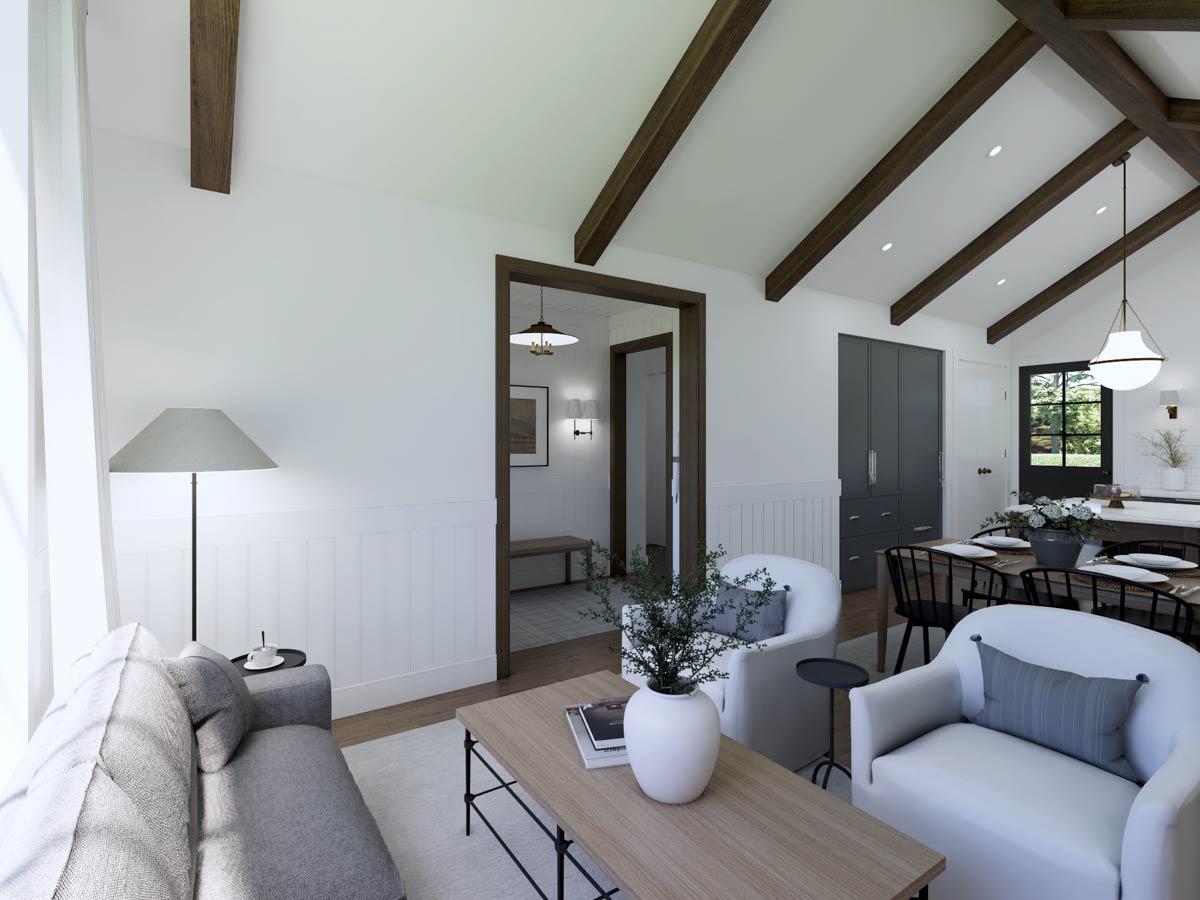 A bright living room with exposed wooden beams, a gray sofa, white armchairs, and a wooden coffee table, leading into a dining area.