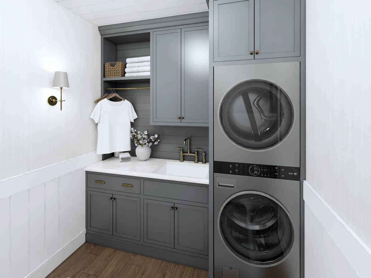 A modern laundry room features a stacked washer and dryer, gray cabinetry, a white sink, and a white t-shirt hanging on a rack. 