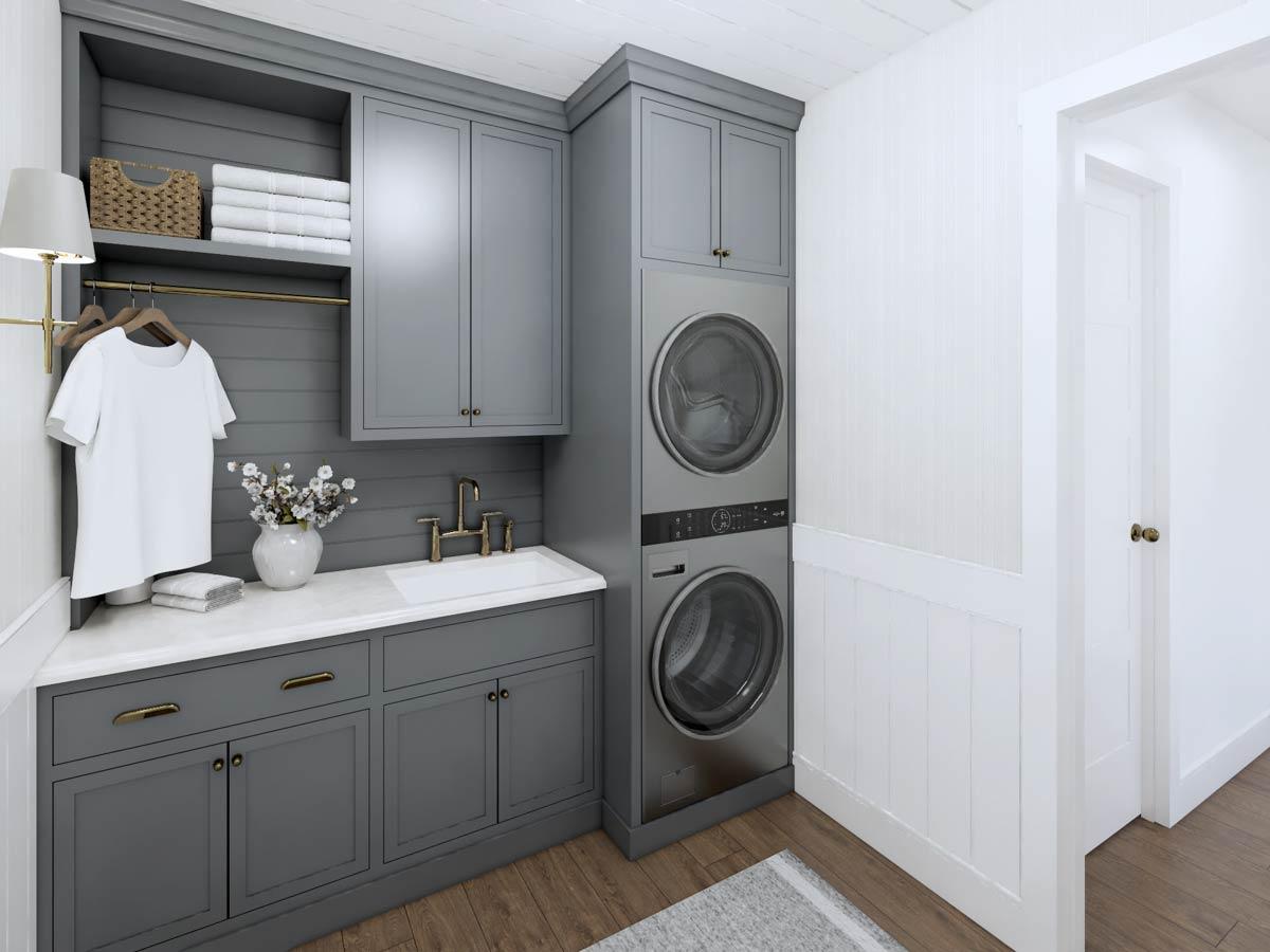 A modern laundry room with a stacked washer and dryer unit, gray cabinets, a white sink, and a white t-shirt hanging on a rack.