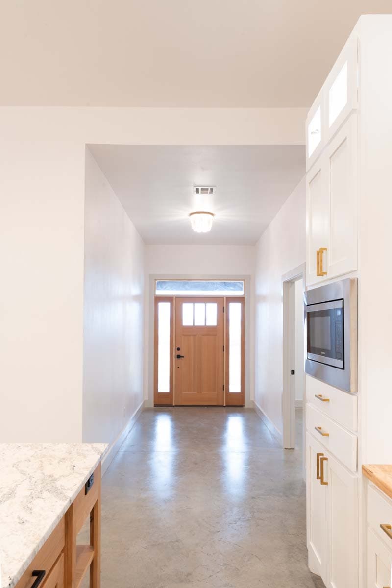 Entryway with natural wood door, sidelights, transom window, concrete floors, and white cabinets with built-in microwave.