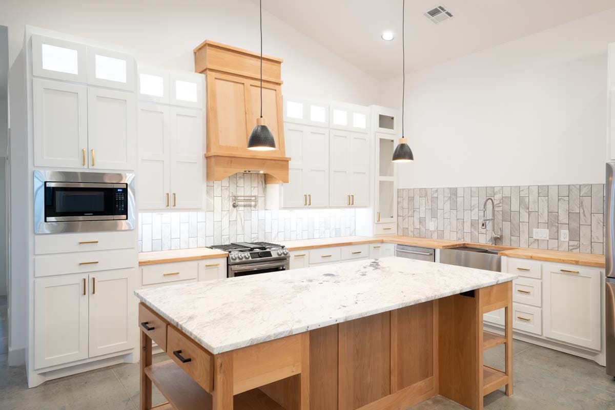 Modern kitchen with white Shaker cabinets, wood range hood, island with granite countertop, and stainless steel appliances.