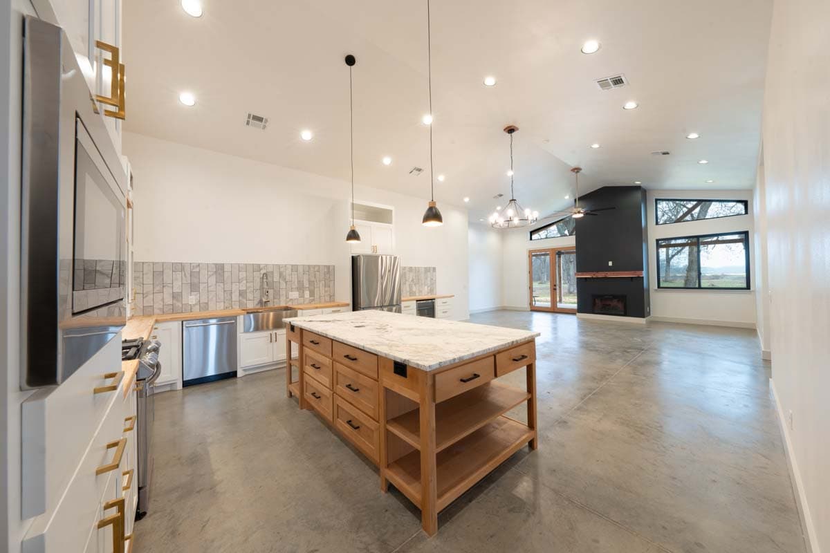 Open concept kitchen and great room with large island, fireplace, and large windows.