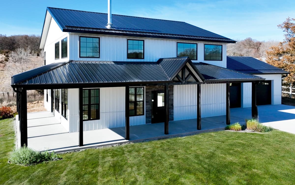 House plan exterior: Modern Farmhouse style, two stories, white board and batten siding, black metal roof, wrap-around porch, and attached garage.