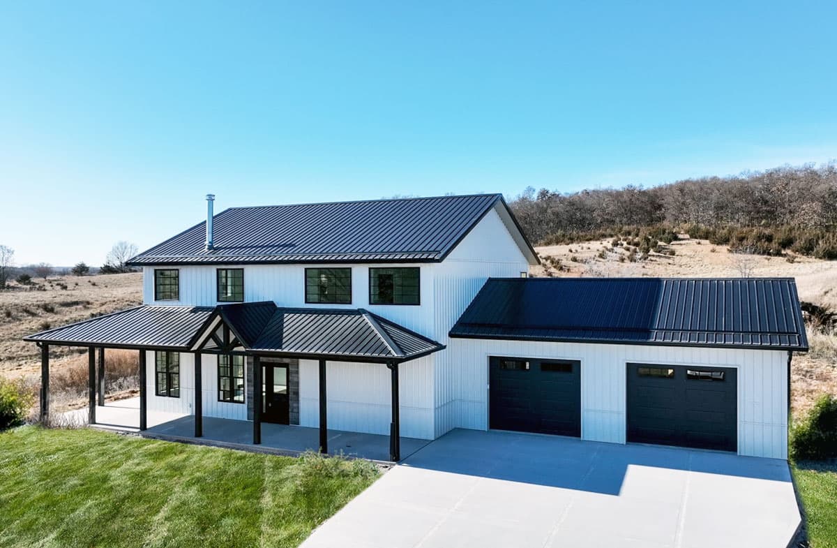 Modern Farmhouse style house plan exterior with white vertical siding, black metal roof, wraparound porch, and attached two-car garage.
