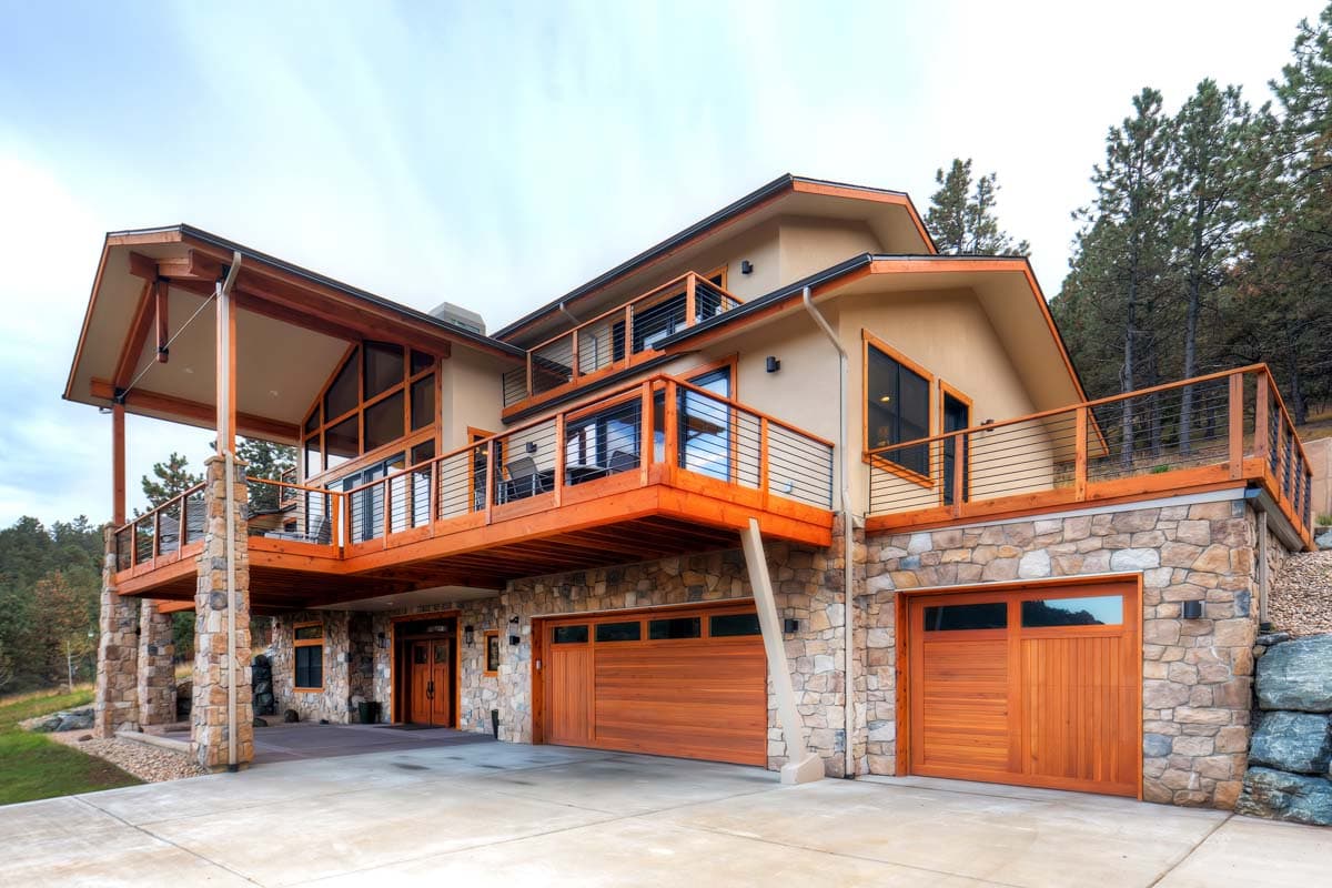 House plan exterior, multi-level contemporary home with stone base, wood siding, large decks, and multiple garage doors.