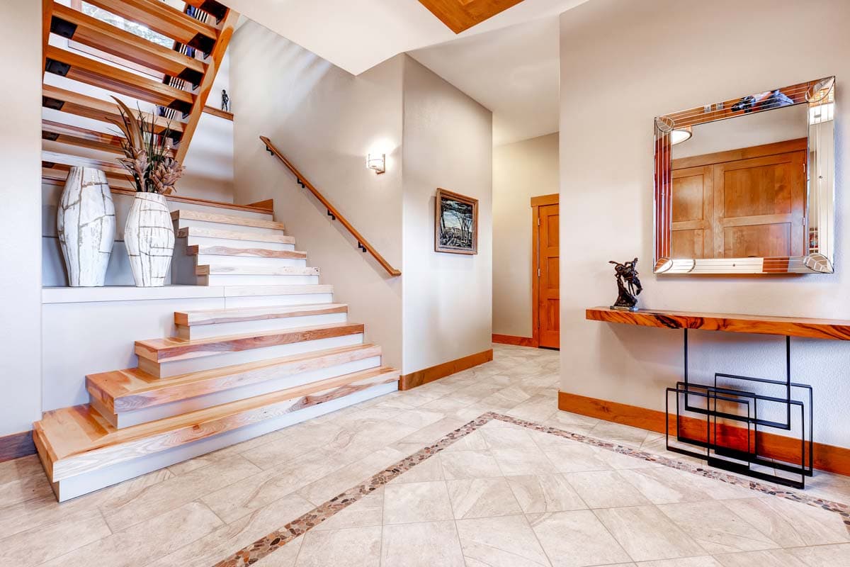 Interior view of a home foyer with a cantilevered wood staircase, decorative tile flooring, console table, and mirror.
