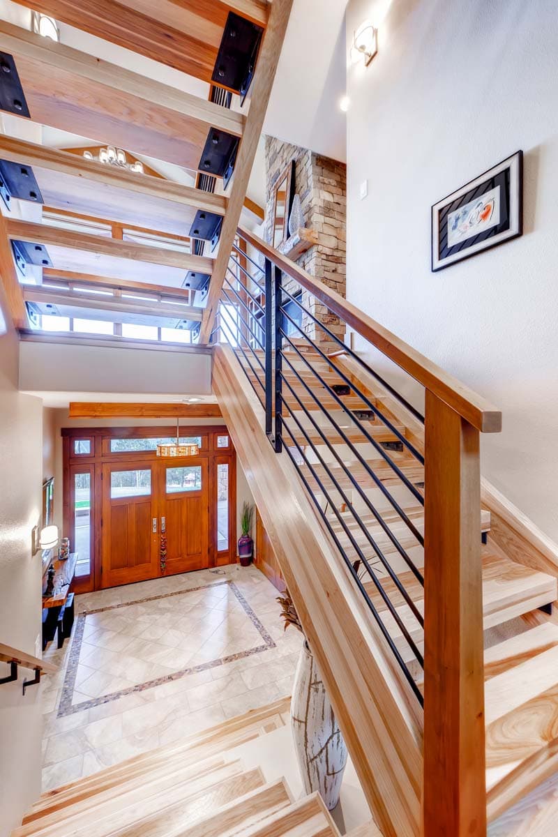 Interior view of entryway with wood double doors, stone fireplace, and open staircase with wood treads and black metal railing.