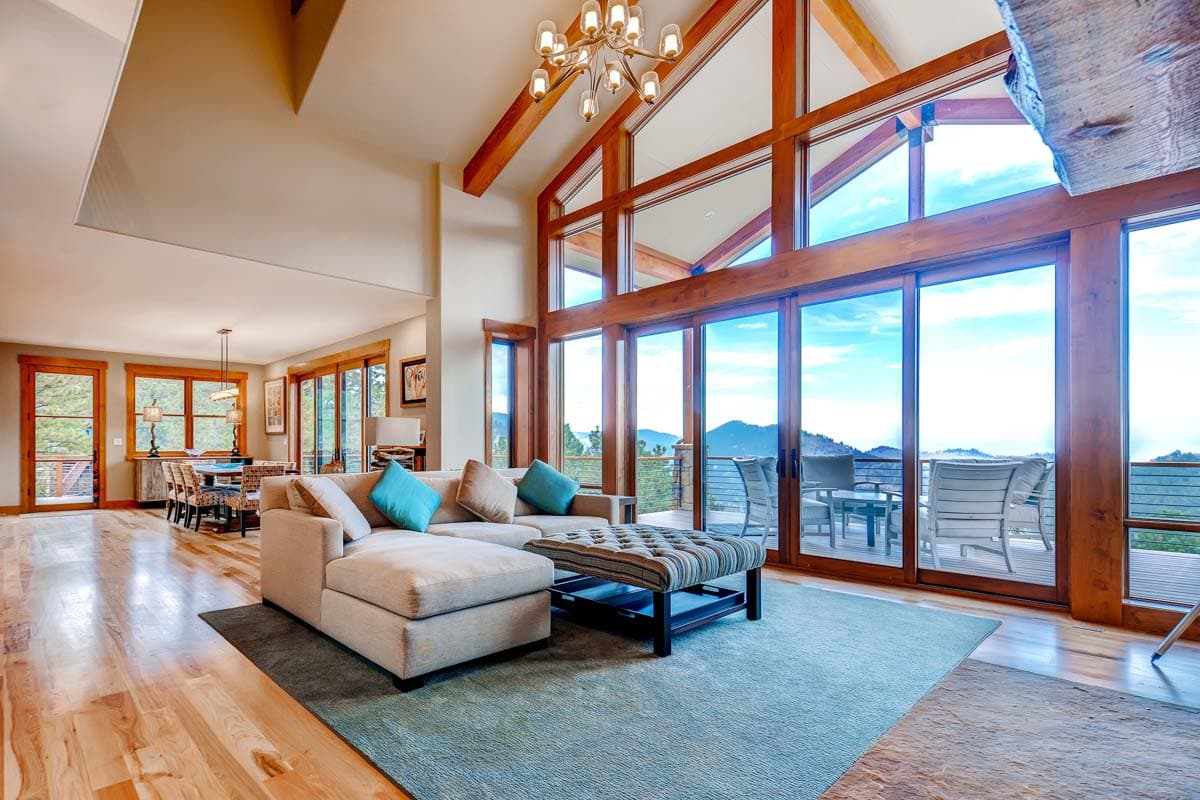Living room with vaulted beamed ceiling, sectional sofa, and floor-to-ceiling windows overlooking mountains.