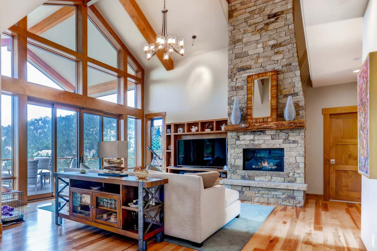 Great room with vaulted ceiling, exposed wood beams, stone fireplace, and large windows.