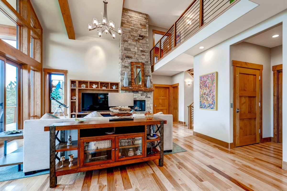 Interior view of great room with stone fireplace, vaulted ceiling with exposed beams, and second-story balcony.