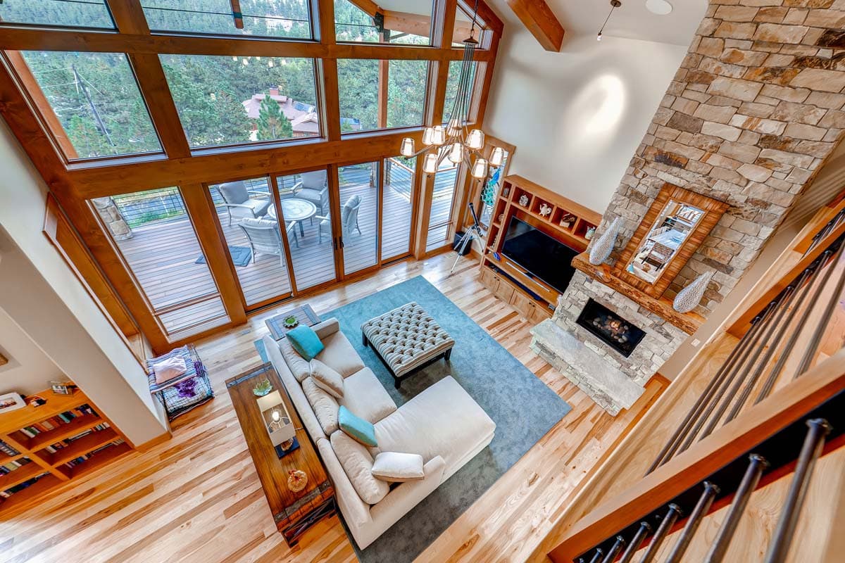 Interior view of a great room with a stone fireplace, floor-to-ceiling windows, and a deck visible.