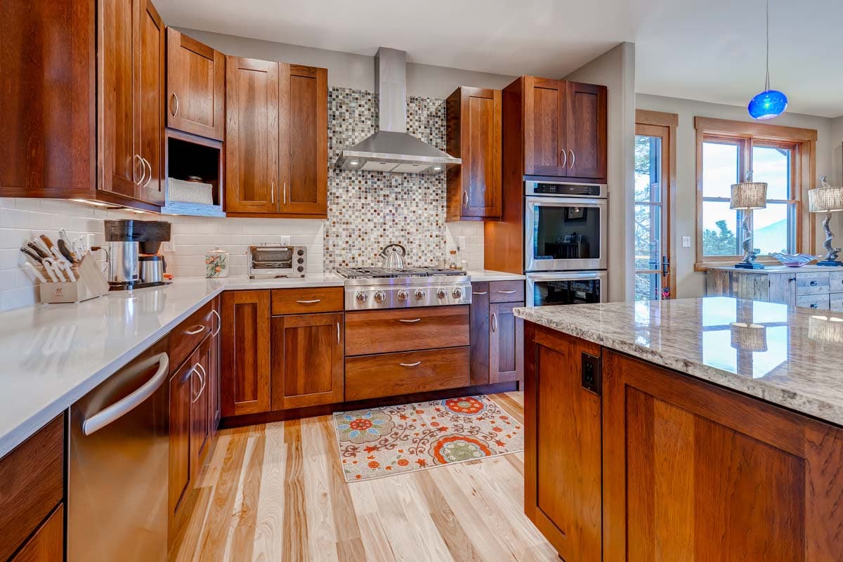 Kitchen with wood cabinetry, stainless steel appliances including double ovens and gas range, and granite-topped island.