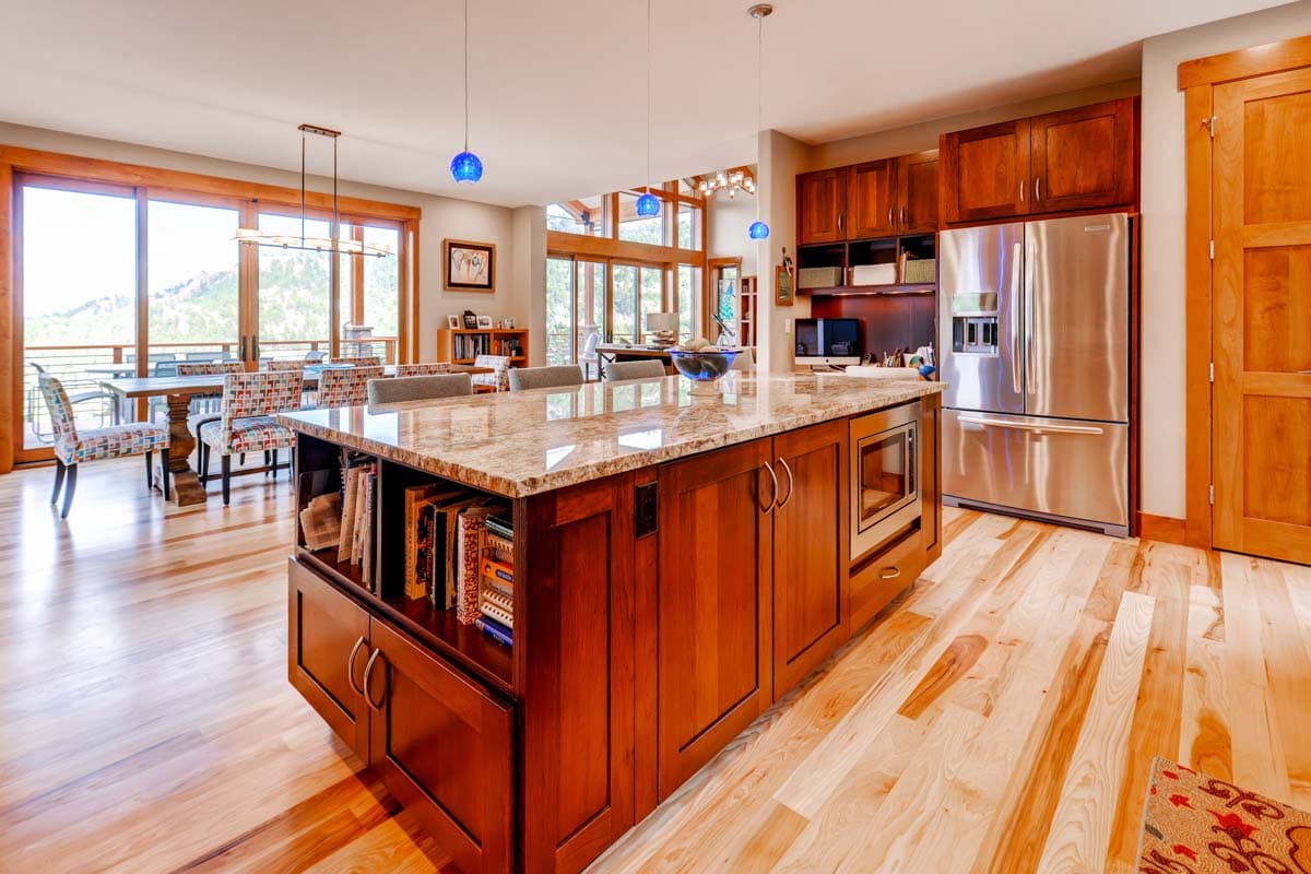 Kitchen with wood cabinetry, granite island with microwave and bookshelf, stainless steel refrigerator, and dining area.