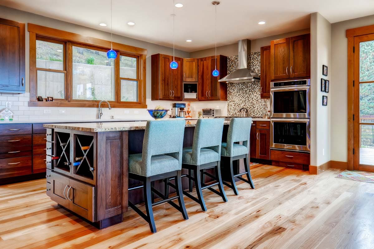 Kitchen with wood cabinetry, island with wine rack, granite countertop, tile backsplash, and stainless steel appliances.