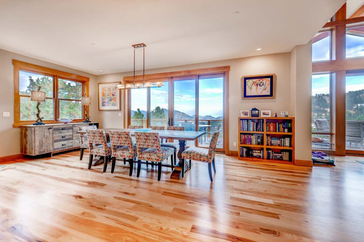Dining room with wooden floors, large windows, built-in bookshelf, and pendant lighting.