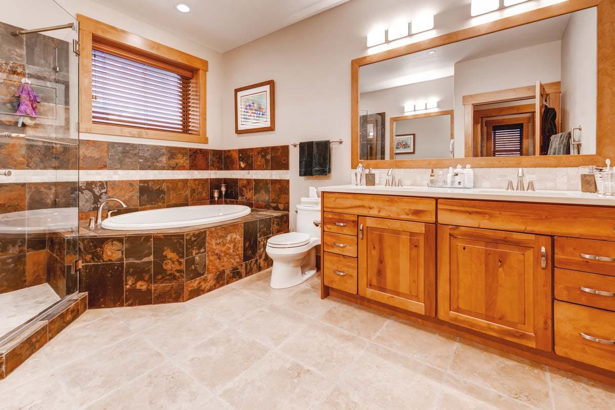 Bathroom interior featuring a soaking tub, glass-enclosed shower, double vanity with wood cabinetry, and stone tile accents.
