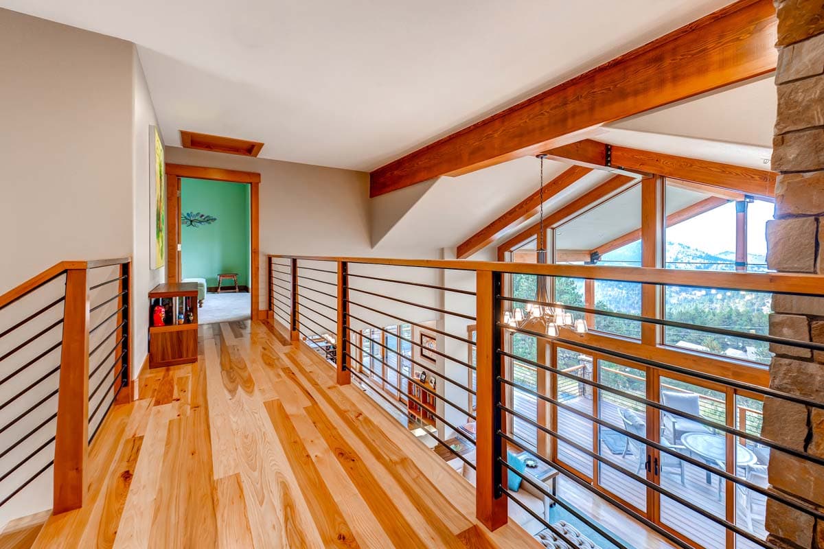 Interior hallway with wood floors, wood railings, exposed wood beams, and a stone fireplace.