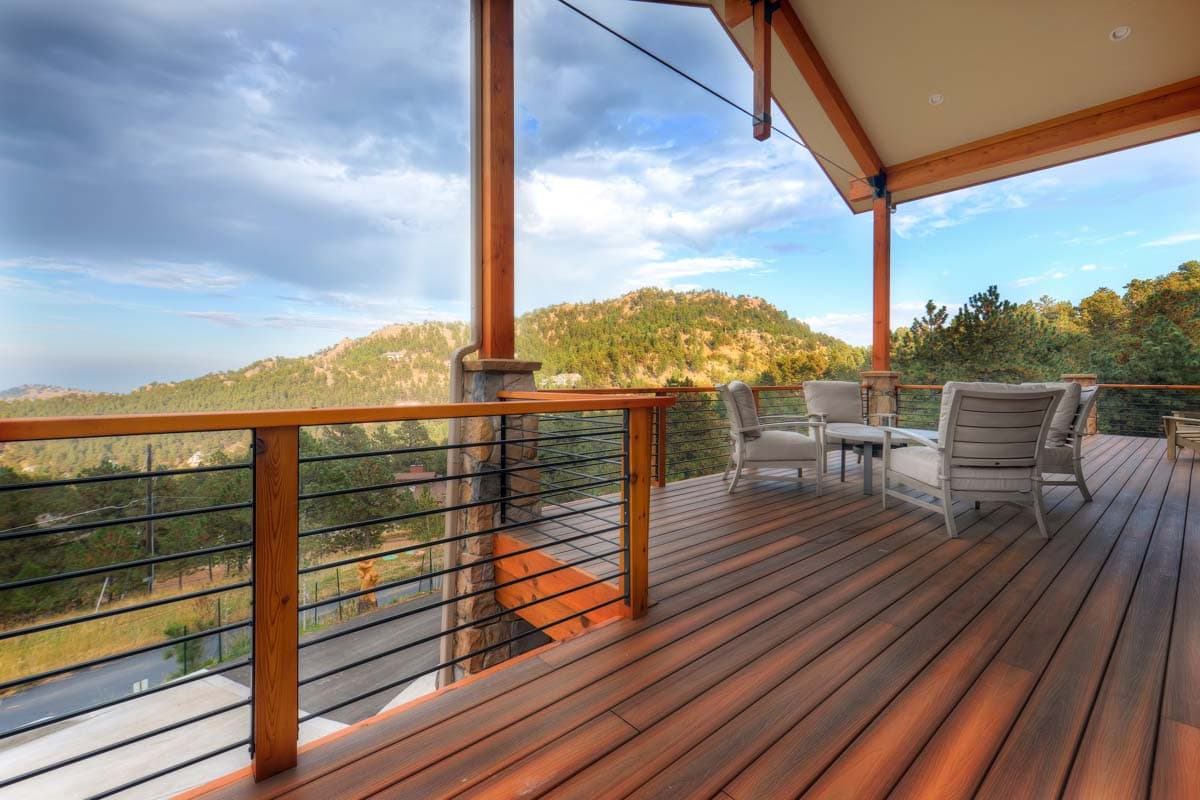 Covered deck with wood decking, stone and wood pillars, and cable railing offers mountain views.