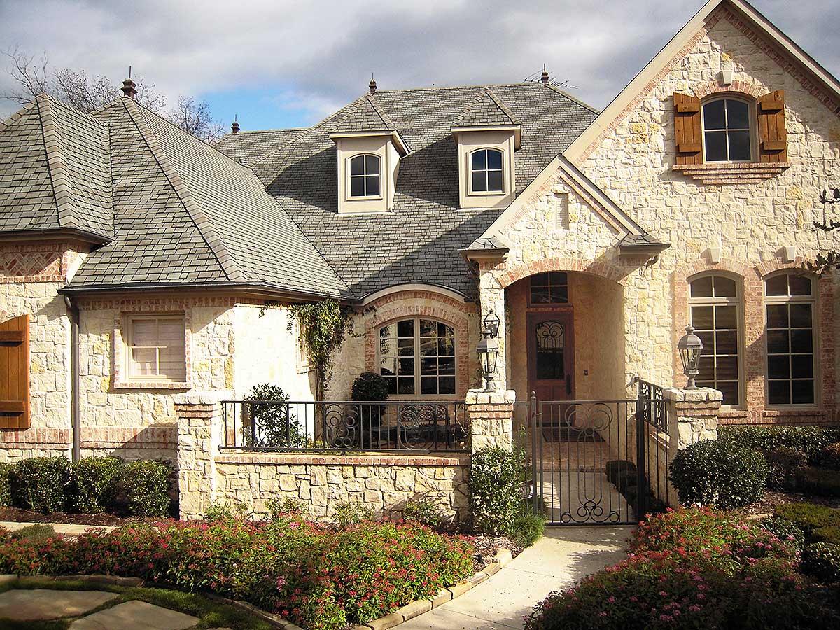 House plan exterior: Stone and brick facade with arched entry, multiple gables, dormers, and decorative shutters.
