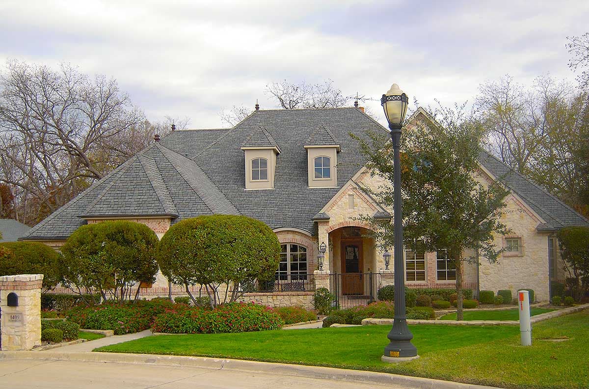 House plan exterior: Stone and brick facade, prominent gables, arched entryway, and two dormer windows.