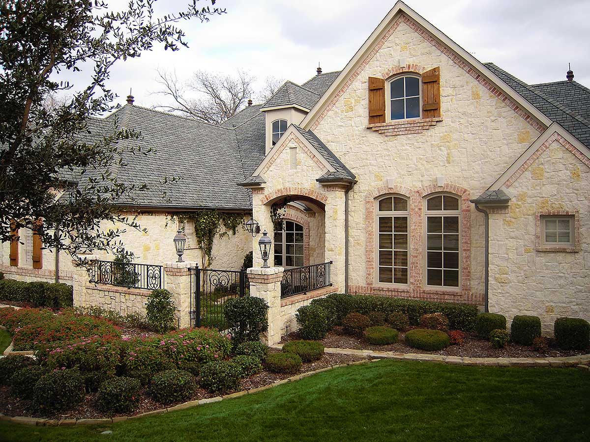 House plan exterior with stone facade, arched windows with shutters, and a covered entry with decorative railing.