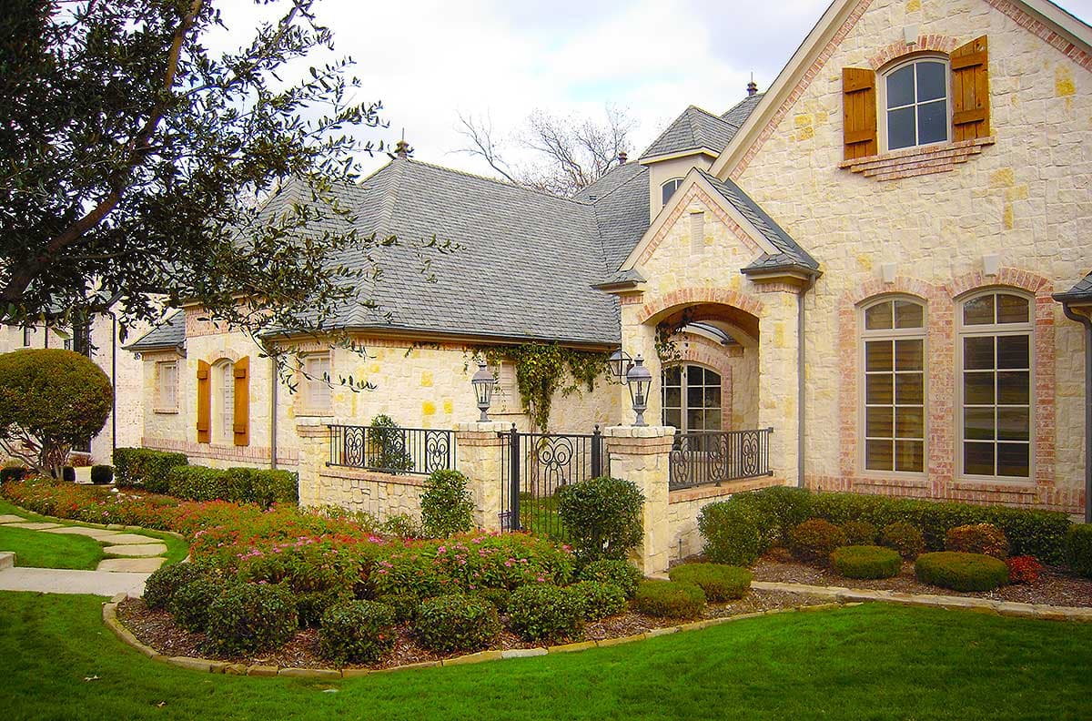 House plan exterior: Two-story stone home with arched entryway, decorative shutters, and multi-level rooflines.