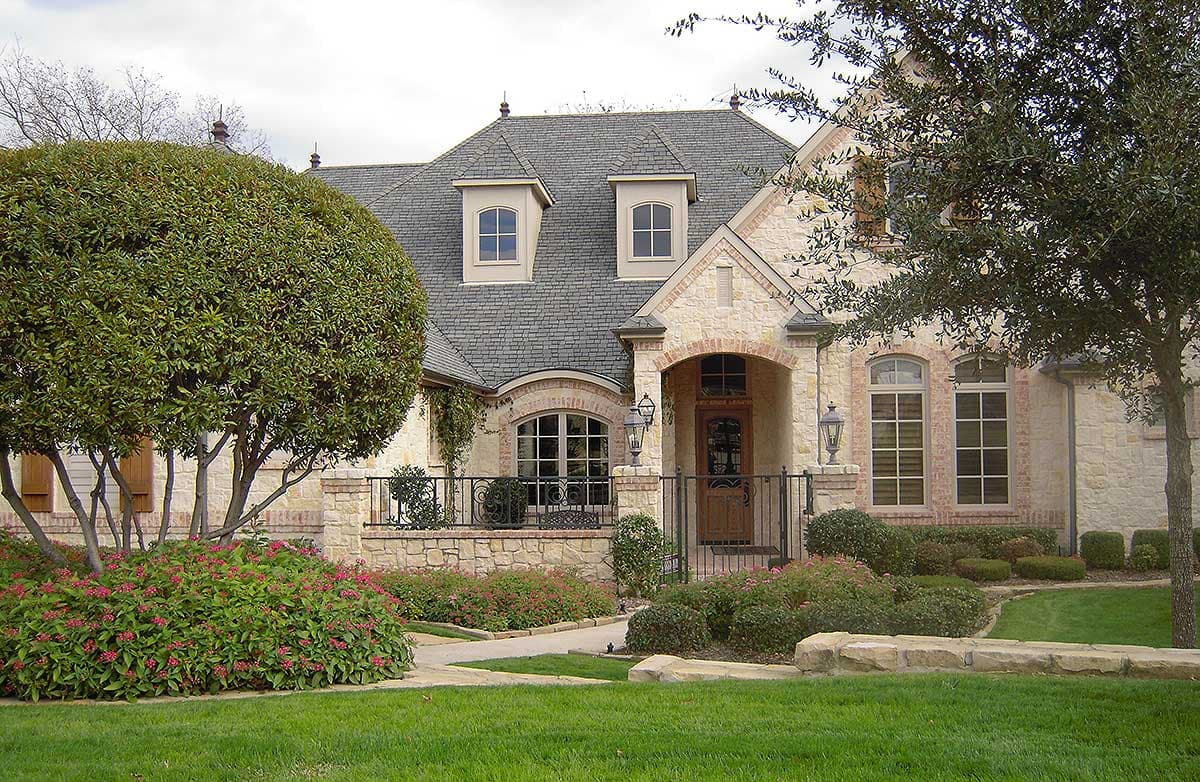 House plan exterior with stone facade, arched entry, two dormers, and steep rooflines.