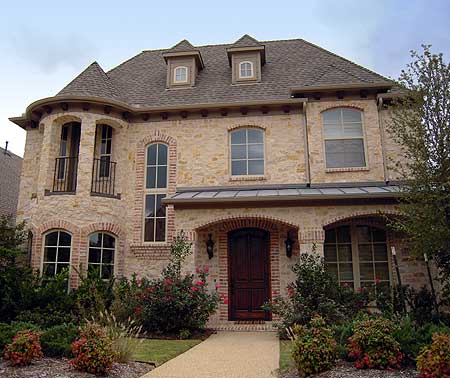 House plan exterior: Two-story home with stone facade, arched entryway, dormers, and balcony with wrought iron railing.