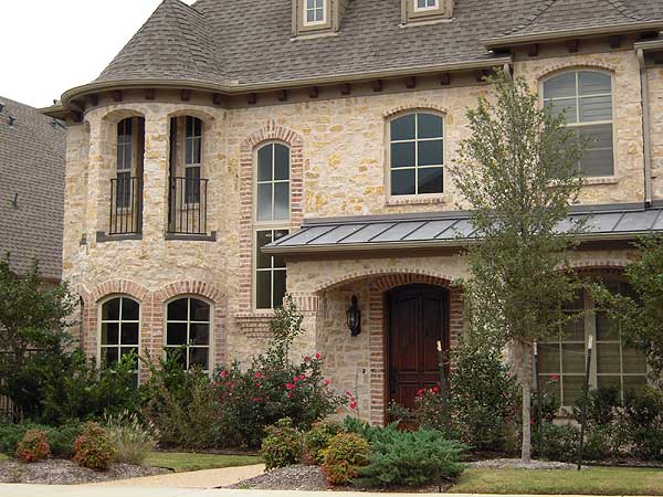 House plan exterior featuring stone facade, arched windows, turrets, and a metal roof over the entrance.