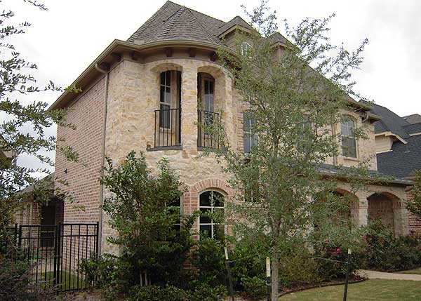 House plan exterior: Two-story home with brick and stone facade, arched entryway, and circular bay window with balconies.