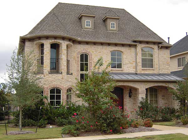 House plan exterior: Two-story stone home with arched windows, dormers, and a covered arched entryway.