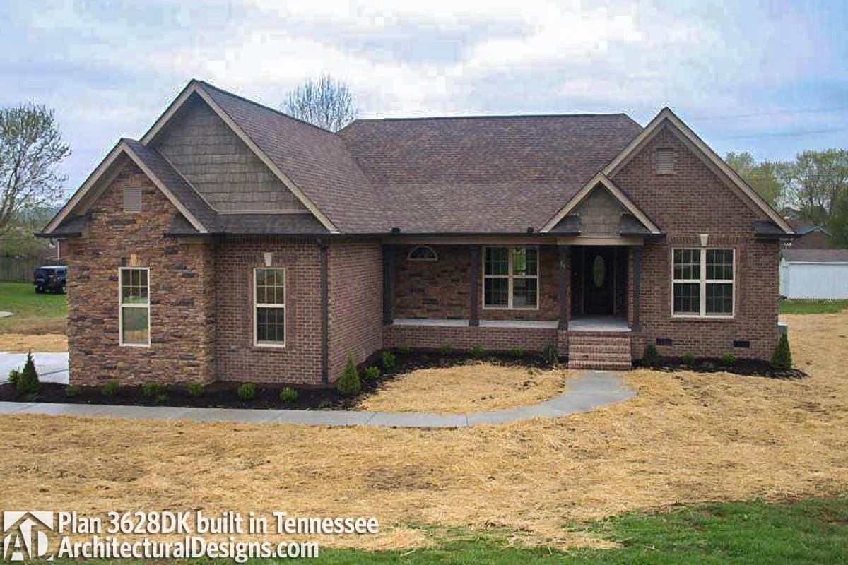 House plan exterior: One-story brick home with stone accents, a covered porch with columns, and multiple gables.