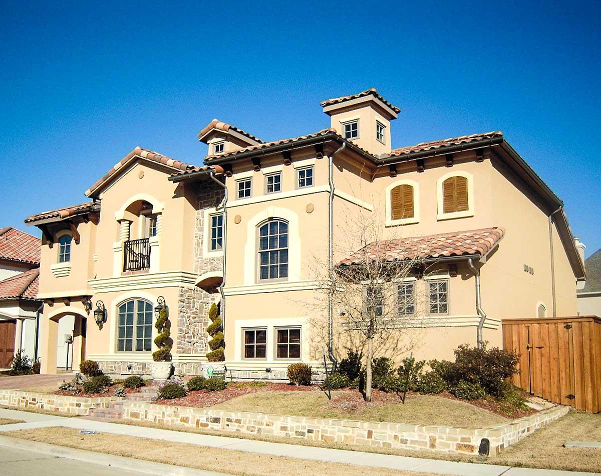 House plan exterior: Tuscan style, three stories, stucco finish, arched windows, tile roof, and covered balcony.