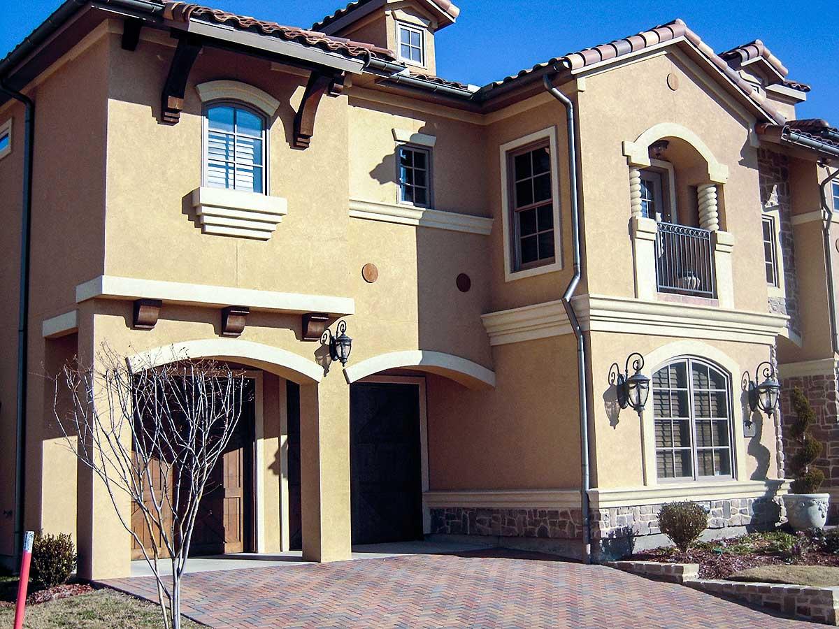 House plan exterior with stucco finish, arched entryway, decorative brackets, and a balcony with railing.