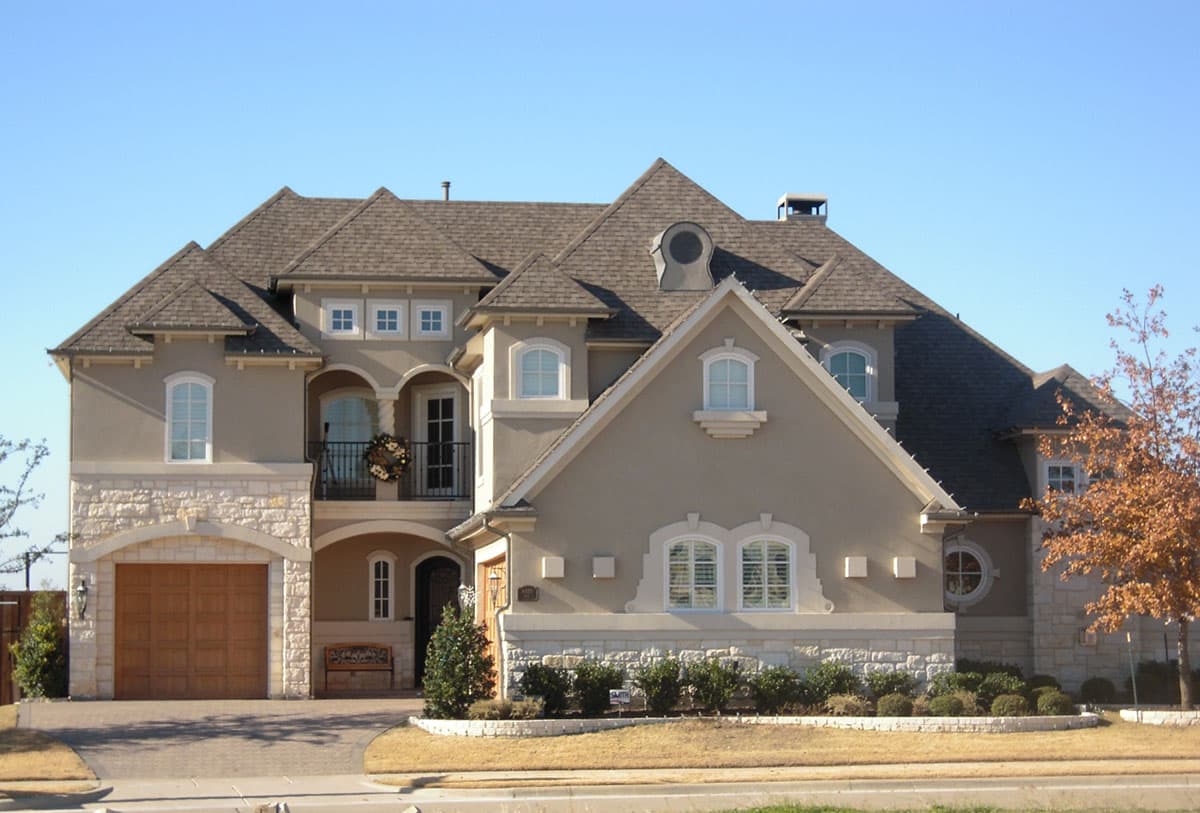 House plan exterior: Two-story home with stone accents, arched garage door, multiple gables, and a second-story balcony.