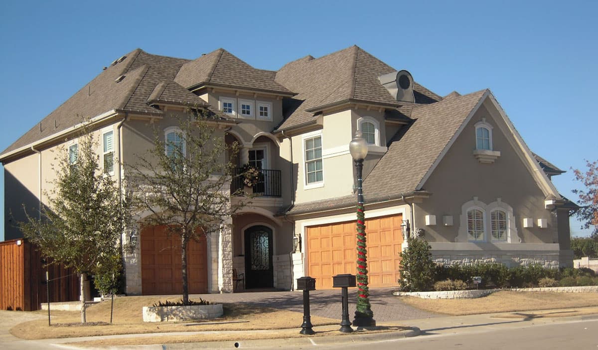 House plan exterior, two stories, with multiple gables, arched entryway, and a balcony above the garage.