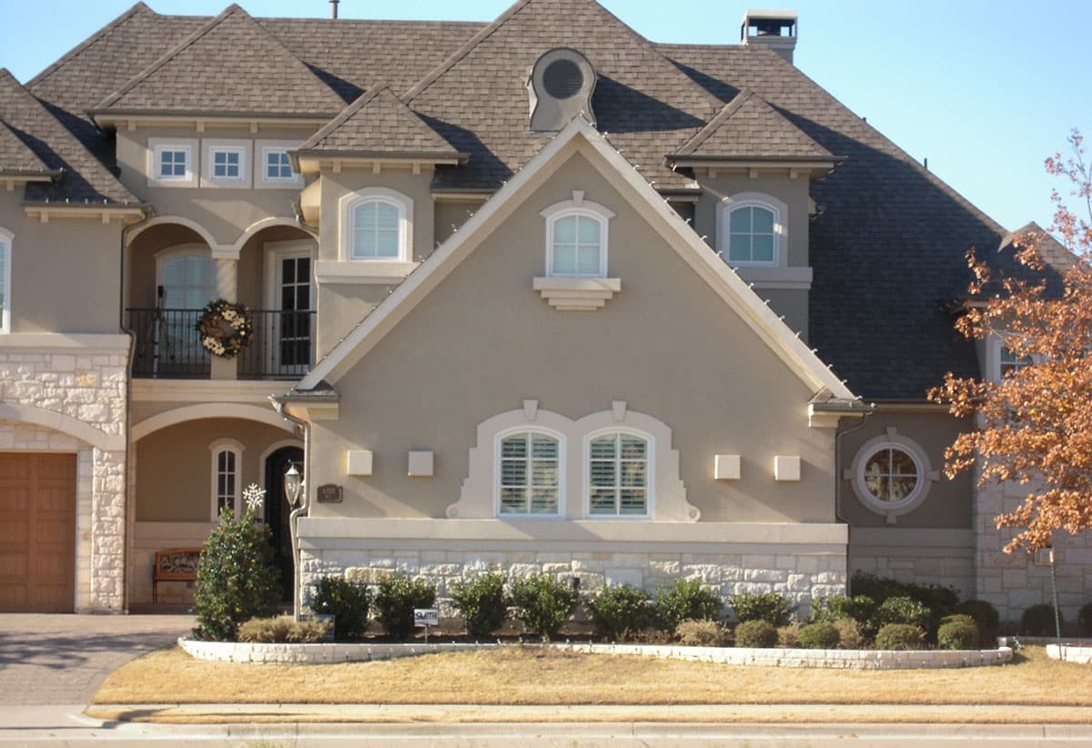 House plan exterior featuring a multi-story stucco facade with stone accents, arched windows, a second-story balcony, and prominent gables.