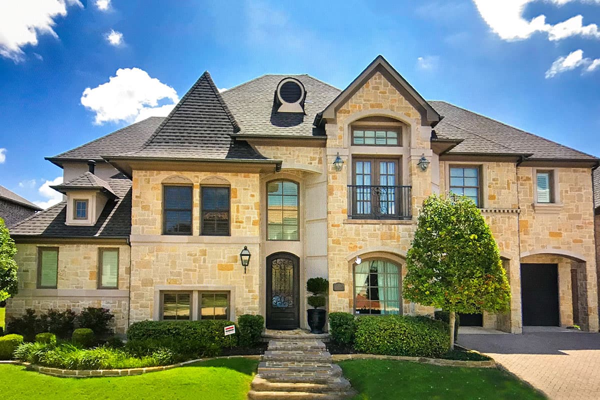 House plan exterior featuring a two-story stone facade with a gable roof, eyebrow dormer, arched windows, and a balcony.