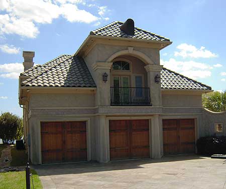 House plan exterior featuring a tile roof, arched balcony, and three wood garage doors. Stucco finish.
