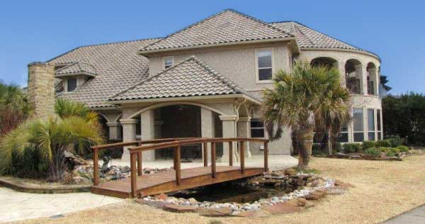 Two-story house plan exterior with arched loggia, tiled roof, stone chimney, and covered entryway.